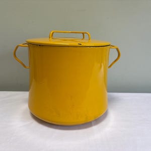 May include: A bright yellow enamel stockpot with a matching lid. The pot features two side handles and a central handle on the lid. The cylindrical body has a smooth finish and a flat base, providing a simple and functional design for kitchen use.