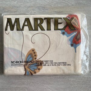 Op de afbeelding: Een Martex eenpersoons laken in de originele plastic verpakking. De gebroken witte stof heeft een vlinderprint in rood, blauw en bruin. De tekst op de verpakking luidt: No-Iron Percale, Twin Flat Sheet voor 99 x 190 cm matras, afgewerkte maat 167 x 243 cm.