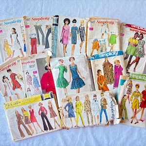 May include: A collection of vintage sewing patterns from Simplicity and McCall's. The patterns feature illustrations of dresses, pantsuits, and other garments. The patterns are in various sizes and styles, with text such as "Simplicity" and pattern numbers visible.