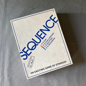 May include: A rectangular box for the game "Sequence" is displayed. The box is white with blue text that reads "SEQUENCE" and "AN EXCITING GAME OF STRATEGY". The box also has text that reads "IT'S FUN, IT'S CHALLENGING, IT'S EXCITING, IT'S SEQUENCE".