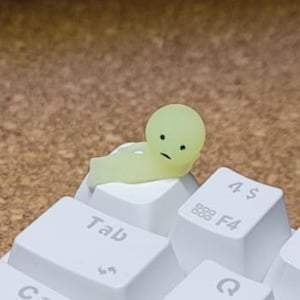 May include: A small, yellow, rubber figurine of a person with a sad expression, lying on a white keyboard with the keys "Tab" and "F4" visible.