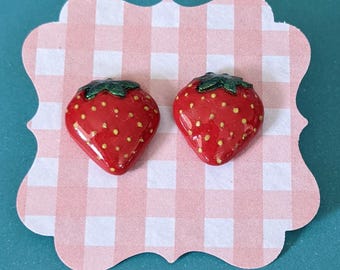 May include: A pair of red and green strawberry stud earrings. The earrings are made of polymer clay and have a glossy finish.