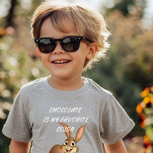 Könnte beinhalten: Ein graues T-Shirt mit einem Comic-Hasen, der ein Schokoladeneier hält. Der Text auf dem Shirt lautet "Chocolate is my favorite color."