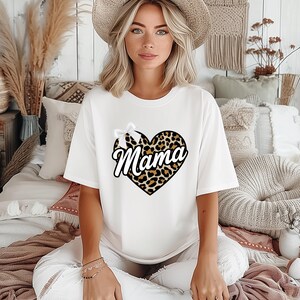 Könnte beinhalten: Weißes T-Shirt mit einem Leopardenmuster-Herz, auf dem "Mama" in weißer Schrift steht.