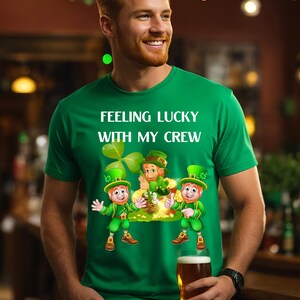 Könnte beinhalten: Grünes T-Shirt mit dem Text "Feeling Lucky With My Crew" und einem Cartoon-Bild von drei Kobolden, die einen Topf Gold halten.