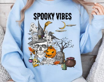 May include: Light blue sweatshirt with a Halloween-themed graphic. The design includes a skull, witch hat, pumpkin, ghost, and the words "Spooky Vibes". The graphic is in black, white, orange, and purple.