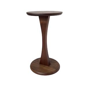 May include: A dark brown, wooden side table with a round top and base, connected by a curved, hourglass-shaped support. The table is approximately 61 cm tall and 36 cm in diameter.
