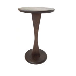 May include: A dark brown, wooden side table with a round top and base. The table's stem has an hourglass shape. The table is a stylish accent piece for any room, measuring approximately 20 inches in height.