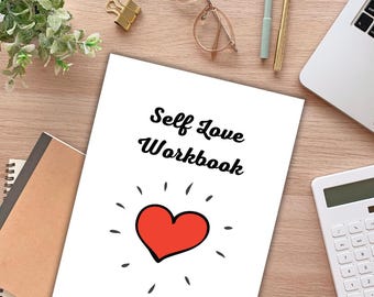 May include: A white workbook titled "Self Love Workbook" with a red heart illustration on the cover. The workbook is on a wooden desk with office supplies, including a laptop, calculator, and glasses. A small plant and gold binder clips are also visible.