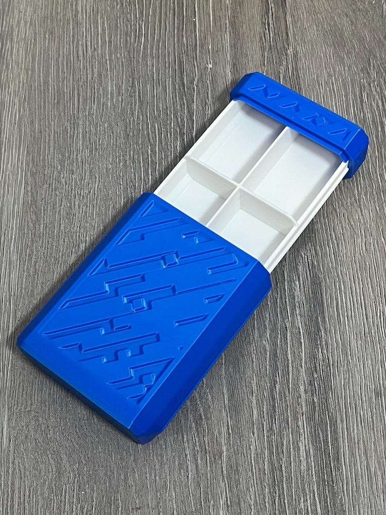 May include: A blue plastic organizer with a sliding lid. The lid and base are a vibrant blue, while the interior features four white compartments. The lid has a textured design and a series of small, triangular shapes.
