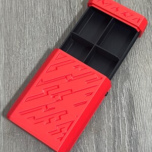 May include: A red plastic box with a sliding lid, featuring a geometric design. The interior is divided into four black compartments. The word "NINJA" is embossed on the top edge of the lid.