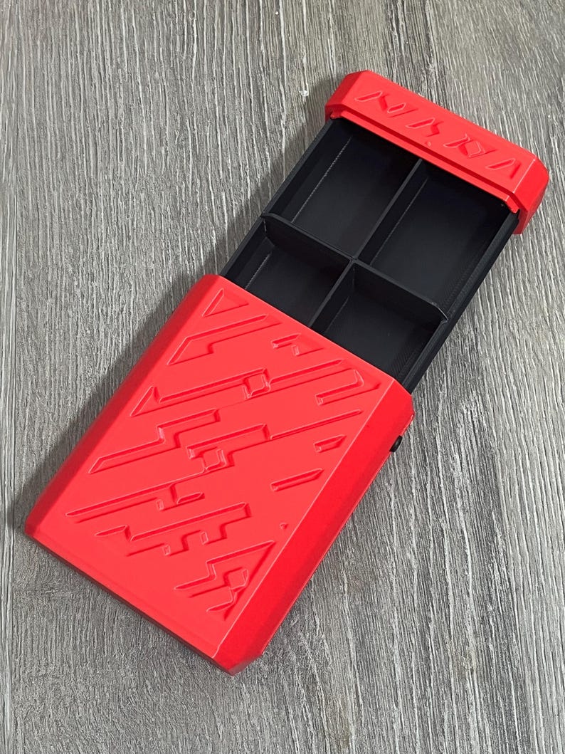 May include: A red plastic box with a sliding lid, featuring a geometric design. The interior is divided into four black compartments. The word "NINJA" is embossed on the top edge of the lid.