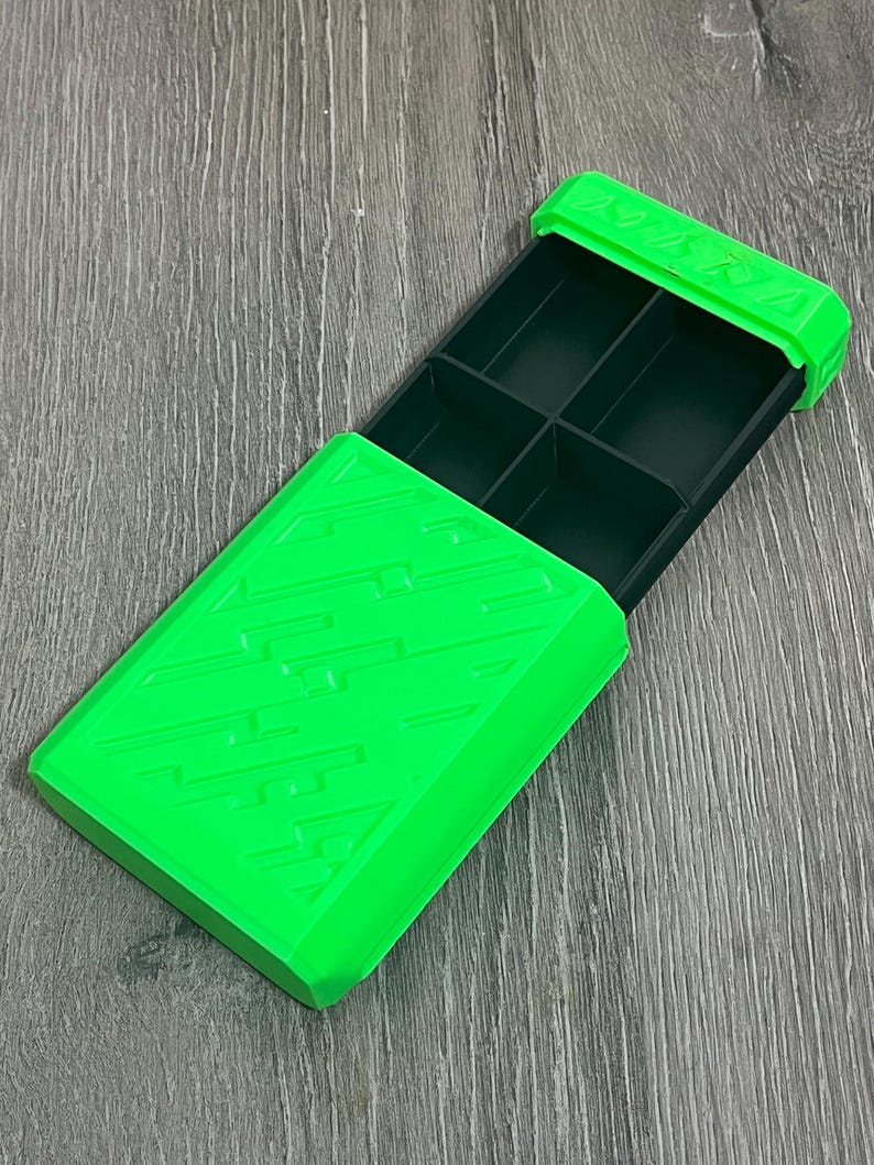 May include: Bright green rectangular storage box with a sliding lid. The box is divided into six compartments. The lid and the box have a textured design. The box is open, revealing the dark green interior.