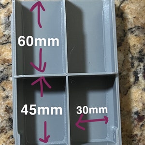 May include: A gray plastic organizer with four compartments. The dimensions are labeled: 60mm high, 45mm wide, and 30mm deep. The organizer is designed to hold small items and keep them separated.