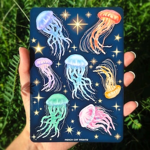 Pu&ograve; includere: Una stampa rettangolare blu scuro con illustrazioni di meduse colorate. Le meduse sono in tonalit&agrave; di rosa, arancione, giallo, verde e blu, con accenti di stelle. Il testo "PEACH CAT PRINTS" &egrave; in basso.