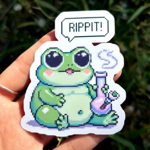 May include: A green frog cartoon sticker with big eyes and a pink tongue holding a purple bong with a speech bubble that says "RIPPIT!"