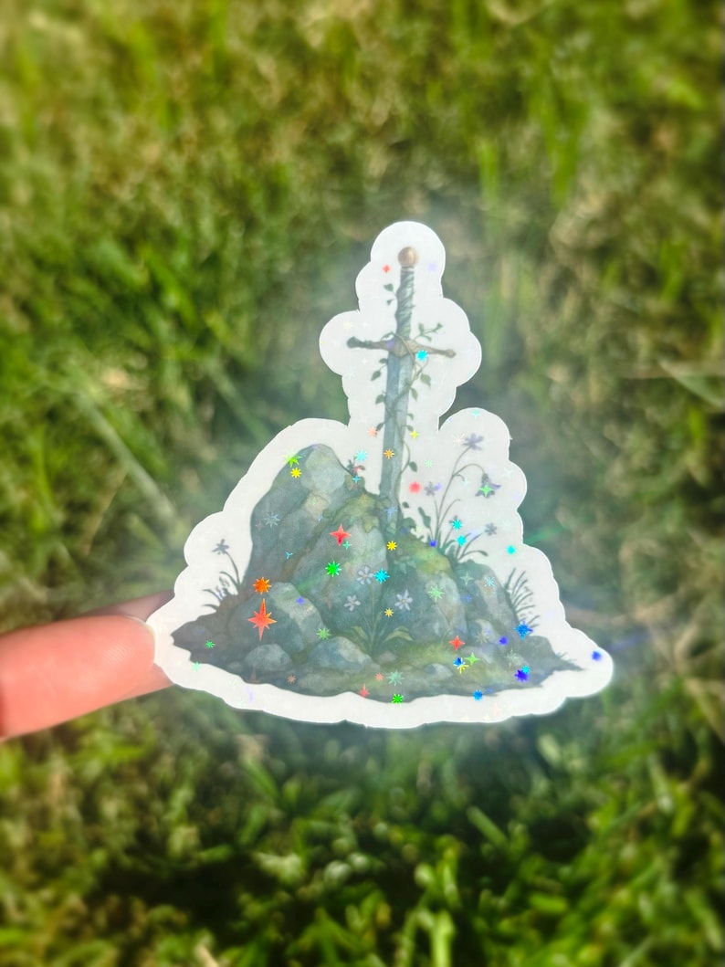 May include: A sticker featuring a sword in a stone design. The sword is adorned with vines and flowers, set against a backdrop of gray rocks and colorful star-shaped accents. The sticker has a holographic finish.