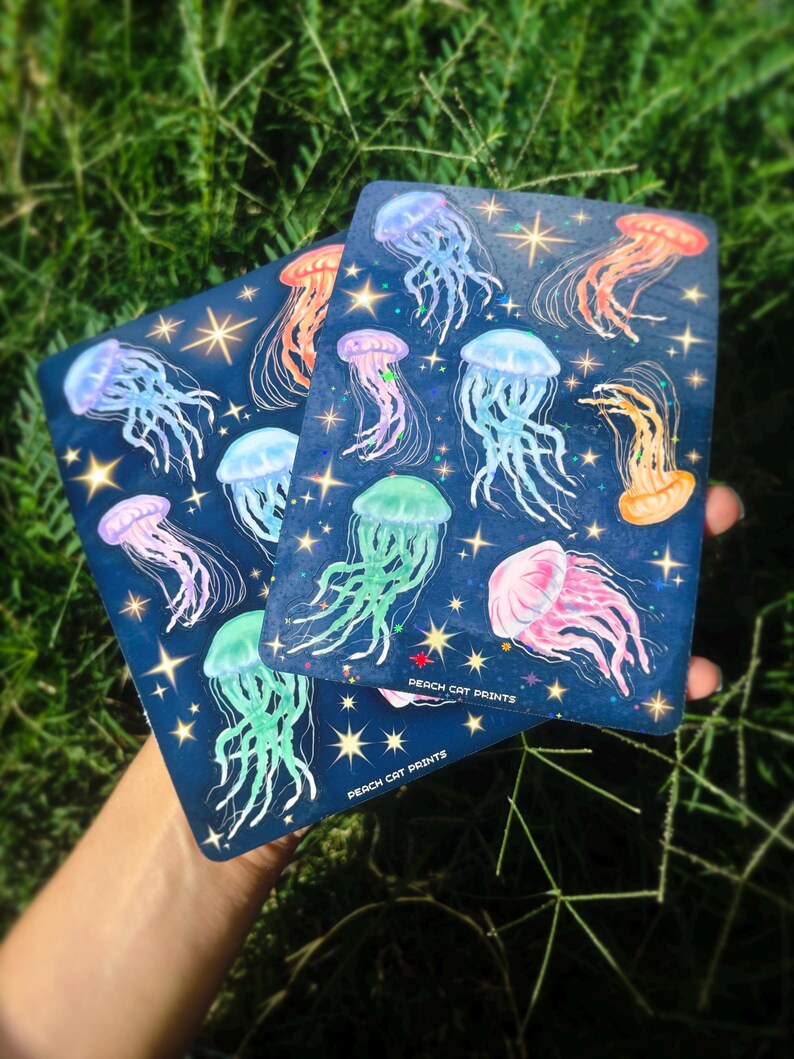 Pu&ograve; includere: Due stampe rettangolari blu navy con illustrazioni di meduse colorate e dettagli di stelle. Le meduse sono in tonalit&agrave; di rosa, blu, arancione e verde. Il testo "PEACH CAT PRINTS" &egrave; stampato in basso su ogni stampa.