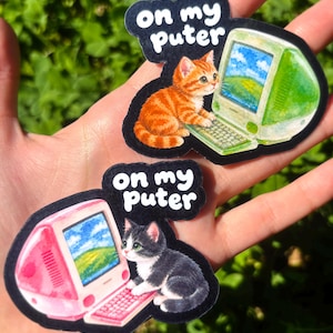 May include: Two die-cut stickers featuring kittens using vintage computers. One sticker shows an orange tabby cat with a green computer, the other a black and white cat with a pink computer. Both display the text 'on my puter' in white.