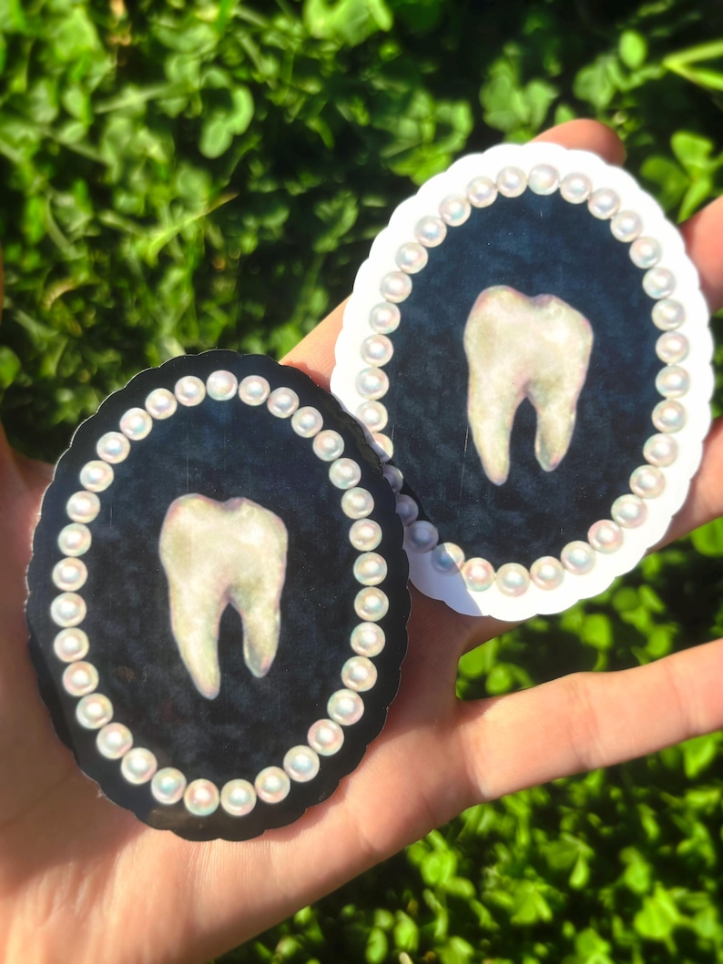 May include: Two oval stickers with a tooth design. One has a black background, the other a white background. Both have a pearl border and a tooth illustration in the centre. The stickers are held in a hand.