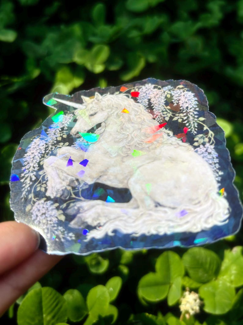 Puede incluir: Una pegatina hologr&aacute;fica que presenta un unicornio blanco con una melena y cola fluidas, rodeado de elementos florales. La pegatina tiene un efecto brillante e iridiscente con acentos coloridos, creando un dise&ntilde;o m&aacute;gico y caprichoso.