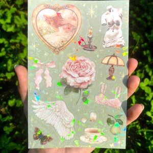 Puede incluir: Una hoja de pegatinas con fondo verde claro y varios dise&ntilde;os. Las pegatinas incluyen un marco en forma de coraz&oacute;n con una pintura, un busto, una rosa, una l&aacute;mpara, una taza de t&eacute;, una mariposa y un ala. El texto "PEACH CAT PRINTS" est&aacute; en la parte inferior.