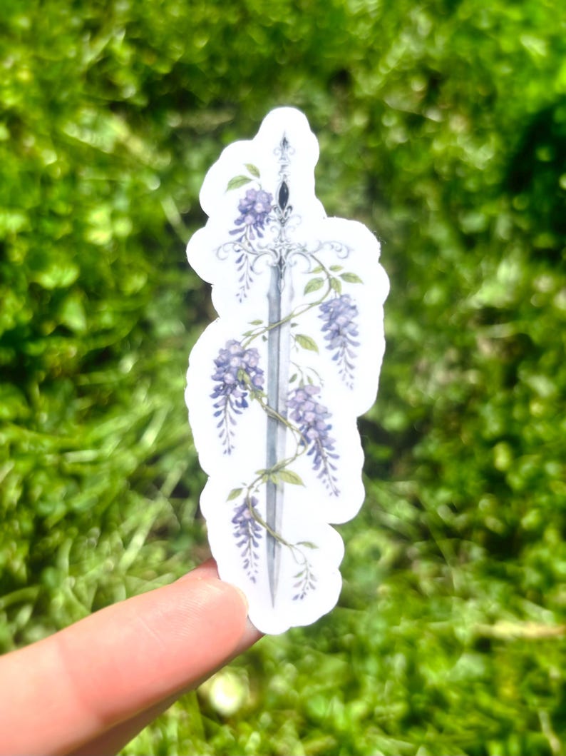 May include: A sticker featuring a detailed illustration of a sword entwined with purple wisteria flowers and green leaves. The sword has a silver blade and ornate hilt. The sticker is on a white background.