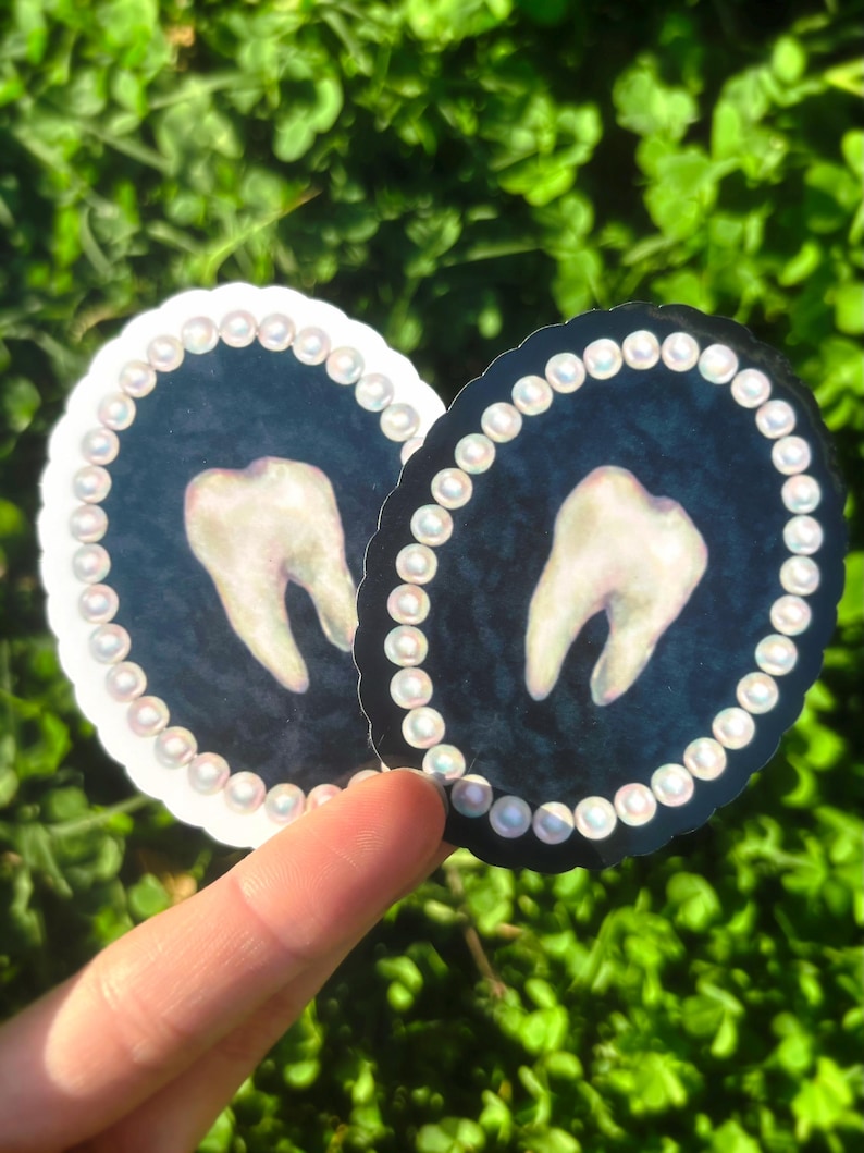 May include: Two round stickers with a tooth design. Each sticker has a dark blue background, a white tooth, and a border of white pearls. One sticker has a white border, the other a black border.