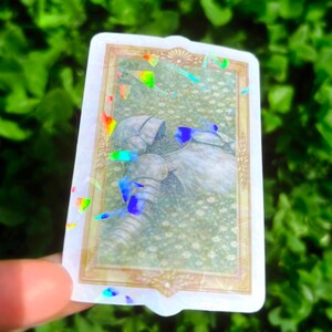Puede incluir: Una pegatina rectangular con borde y detalles hologr&aacute;ficos. La pegatina presenta una ilustraci&oacute;n detallada de un caballero con armadura sobre un fondo floral. La imagen tiene una est&eacute;tica vintage, con un marco dorado.