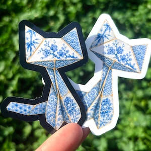 May include: Two fox-shaped stickers featuring a blue and white porcelain-inspired pattern. The design incorporates floral motifs, bamboo stalks, and geometric wave patterns with thin gold-colored outlines, presented on black and white borders.