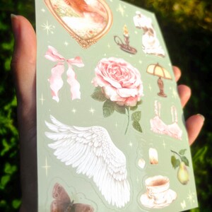 Puede incluir: Una hoja de pegatinas con varias ilustraciones sobre un fondo verde claro. Los dise&ntilde;os incluyen una rosa rosa, una mariposa, un par de alas, un lazo, una imagen en forma de coraz&oacute;n, una taza de t&eacute; y una pera. El texto "PEACH CAT PRINTS" es visible.