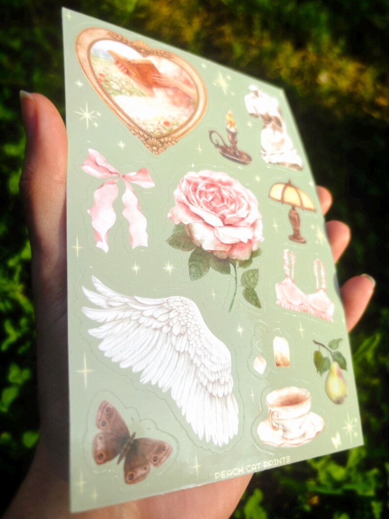 Puede incluir: Una hoja de pegatinas con varias ilustraciones sobre un fondo verde claro. Los dise&ntilde;os incluyen una rosa rosa, una mariposa, un par de alas, un lazo, una imagen en forma de coraz&oacute;n, una taza de t&eacute; y una pera. El texto "PEACH CAT PRINTS" es visible.