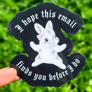 Könnte beinhalten: Ein schwarzer Aufkleber mit einer weißen Hasenillustration und dem Text "I hope this email finds you before I do" in gotischer Schrift. Der Hase hat graue Flecken und eine rosa Schleife.
