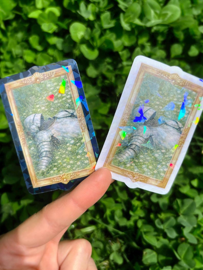 Puede incluir: Dos pegatinas con una armadura de caballero en un campo de flores, enmarcadas en oro. Las pegatinas tienen un efecto hologr&aacute;fico, con colores del arco&iacute;ris visibles. El fondo es un campo de follaje verde.