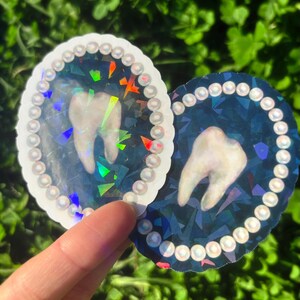 May include: Two oval stickers featuring a tooth design. One has a white background, the other a dark blue. Both have a pearl-like border and a holographic effect. The stickers are suitable for various applications.