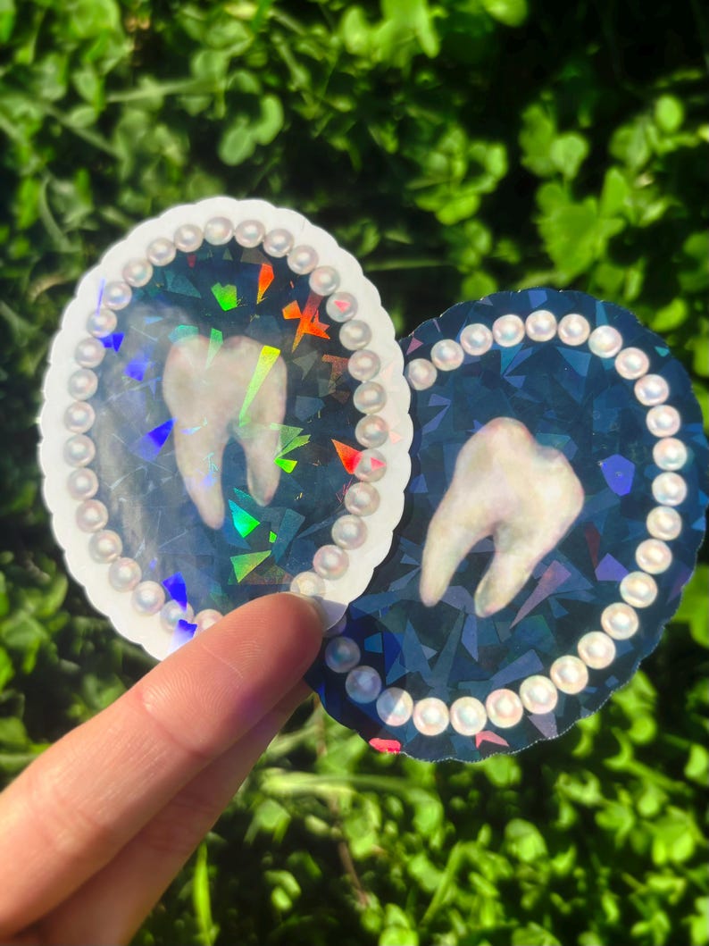 May include: Two oval stickers featuring a tooth design. One has a white background, the other a dark blue. Both have a pearl-like border and a holographic effect. The stickers are suitable for various applications.