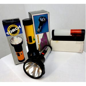 May include: A collection of vintage flashlights and their boxes. One flashlight is yellow and black with a wide beam. Another is black and silver. The boxes feature the words "Torch" and "Wide Beam Krypton Flashlight".