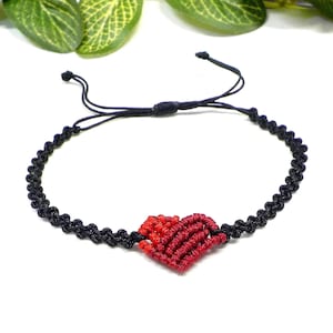 Può includere: Un braccialetto in cordoncino nero con un ciondolo a forma di cuore rosso. Il cuore è realizzato in cordoncino intrecciato e presenta un gradiente di colori rosso e arancione.