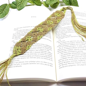 May include: A green and brown woven bookmark with a tassel. The bookmark is lying on an open book.