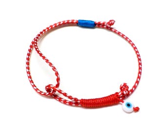 Könnte beinhalten: Rotes und weißes Armband aus Schnur mit einem blauen Akzent und einem blauen Glücksbringer in Form eines bösen Auges.