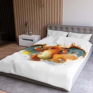 May include: White duvet cover featuring a watercolour illustration of a cartoon orange and blue dragon with flames. The duvet cover is on a bed with grey pillows.