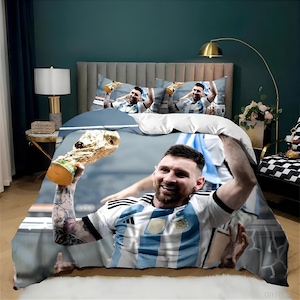 Puede incluir: Un juego de cama azul y blanco con una foto de un jugador de fútbol sosteniendo un trofeo. El jugador lleva una camiseta azul y blanca con el número 10. El juego de cama incluye una funda nórdica, dos fundas de almohada y una sábana bajera.