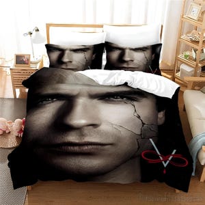 May include: Black and white bedding set featuring a close-up image of a man's face with cracked skin. The bedding set includes a duvet cover, two pillowcases, and a decorative throw pillow. The throw pillow features a red infinity symbol with a red line through it.