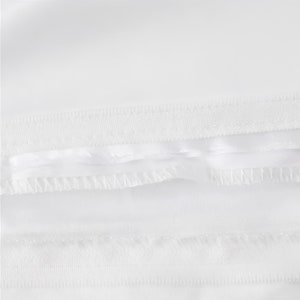 Puede incluir: Primer plano de una tela blanca con una doble fila de costuras a lo largo del borde inferior.