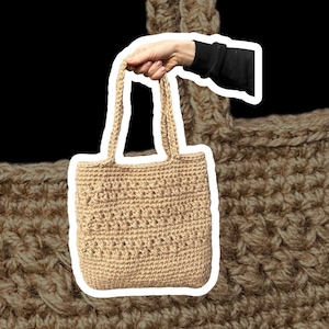 Puede incluir: Un bolso de mano de crochet beige con dos asas. El bolso está hecho de fibras naturales y tiene un diseño simple y elegante.
