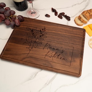 May include: A dark brown wooden cutting board with a floral design and the text "Nana's Kitchen" engraved on it.