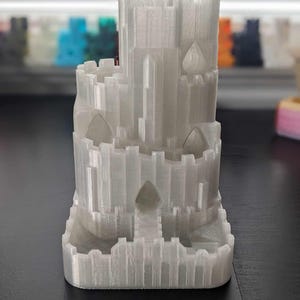 May include: A white 3D printed castle tower with a spiral staircase and multiple windows. The castle is made of a smooth, textured plastic.