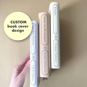 May include: Three hardcover books with custom book cover designs. The spines display the titles "The Two Towers", "Crime and Punishment", and "Lolita". The books are in shades of white and beige, with decorative elements and author names.