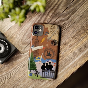 May include: A brown and tan phone case with a colourful design featuring the text "Camp Half-Blood" and a variety of symbols, including a lightning bolt, a sword, and a pegasus. The case also features a building with the text "The Dam Snack Bar".