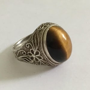 May include: A silver ring with an ornate floral design and a brown tiger's eye gemstone.